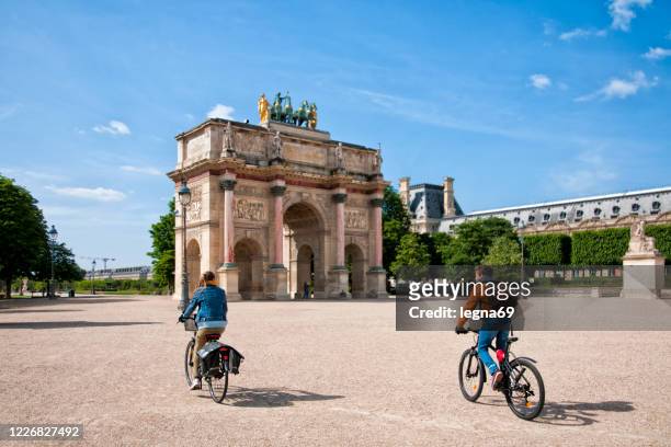 arc de triomphe du carroussel, near louvre with a couple of cyclists - place du louvre stock pictures, royalty-free photos & images