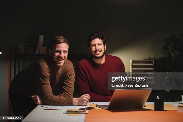 porträt von zwei geschäftsleuten, die spät in der nacht im büro zusammenarbeiten und in die kamera schauen - corporate dark portrait stock-fotos und bilder