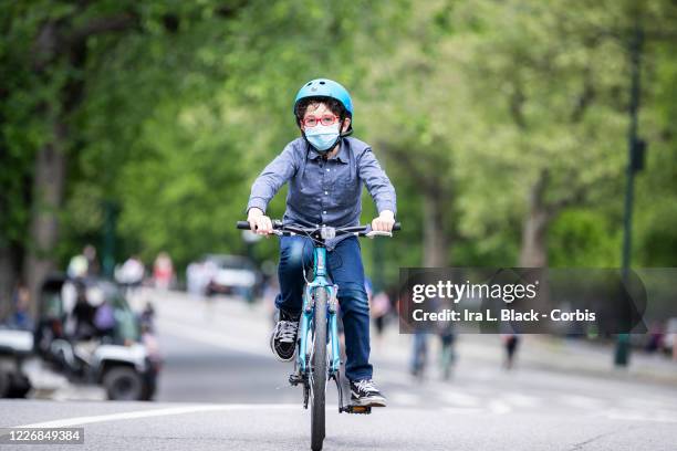 On Memorial Day weekend a child with a mask and glasses rides a bicycle in Central Park with other riders. On May 24, New York State Governor Andrew...