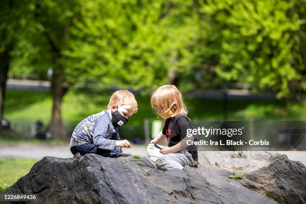 On Memorial Day weekend a two children wear a masks while sitting on the rocks and playing with leaves in Central Park. On May 24, New York State...