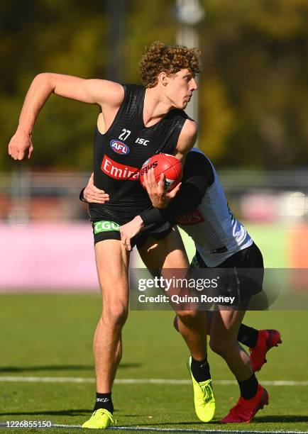 Will Kelly of the Magpies handballs whilst being tackled by John Noble of the Magpies during a Collingwood Magpies AFL training session at Holden...