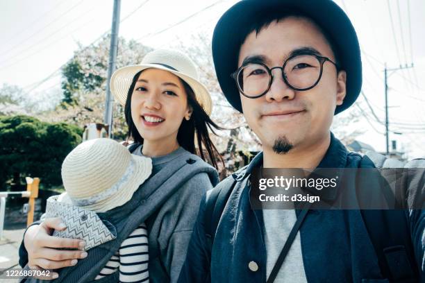 happy young asian family of three taking a selfie, smiling happily while on a trip visiting and exploring a local town in fukuoka, japan on a sunny day - self portrait photography stockfoto's en -beelden