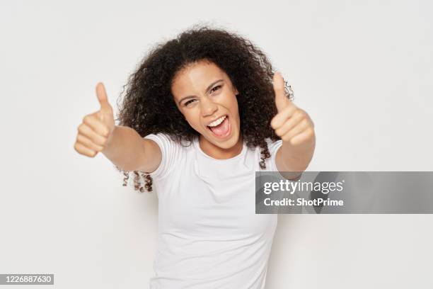 emotional happy woman in a white t-shirt on a gray background shows two thumbs up - black thumbs up white background stock pictures, royalty-free photos & images