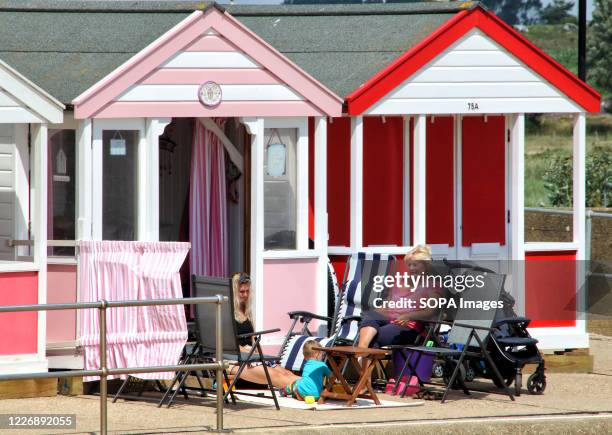 People sit outside their quaint and colourful beach huts at Southwold. With the beaches in England now fully opened with only social distancing...