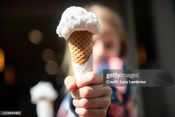 eight year old girl holding two ice cream cones, offering one to the viewer - waffle stock-fotos und bilder