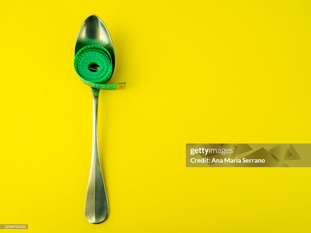 Spoon and measure tape on yellow background. Diet and obesity concept