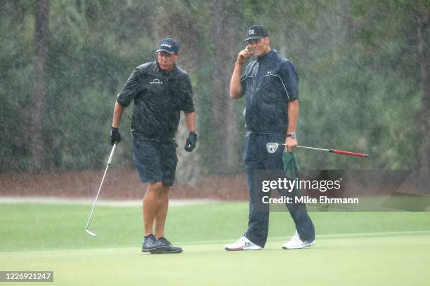 Phil Mickelson and NFL player Tom Brady of the Tampa Bay Buccaneers stand in the rain on the 13th green during The Match: Champions For Charity at...