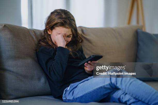 small girl with smartphone sitting indoors on sofa, crying. - cyberbullying stock-fotos und bilder