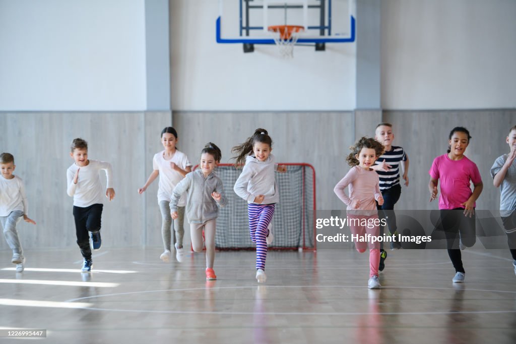 Group of pupils exercising indoors in gym class, running.