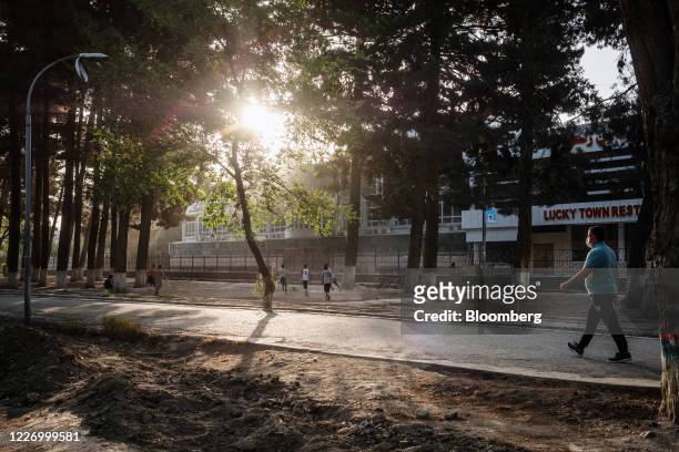 Man wearing a protective mask walks past boys playing football in a park at sunrise in Kabul, Afghanistan, on Sunday, July 12, 2020. Covid-19 is...