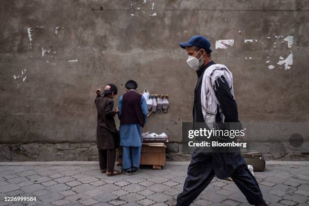 Pedestrian wearing a protective mask walls past boys setting up a street stall selling masks in Kabul, Afghanistan, on Sunday, July 12, 2020....