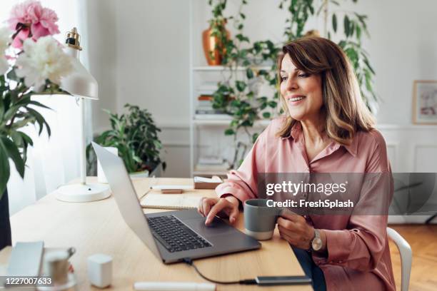 gelukkige hogere zitting van de vrouw in haar bureau van het huis en gebruikend haar laptopcomputer - pink stockfoto's en -beelden