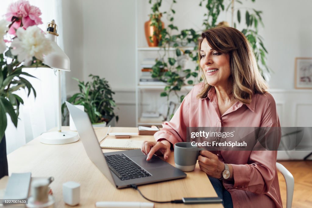 Feliz mulher idosa sentada em seu home office e usando seu laptop computador