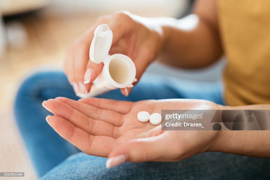 Healthy young woman taking supplements, close up of woman's hand with pills