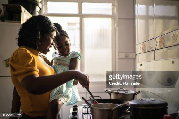 mutter kocht zu hause, während sie ihre tochter hält - brazilian family stock-fotos und bilder