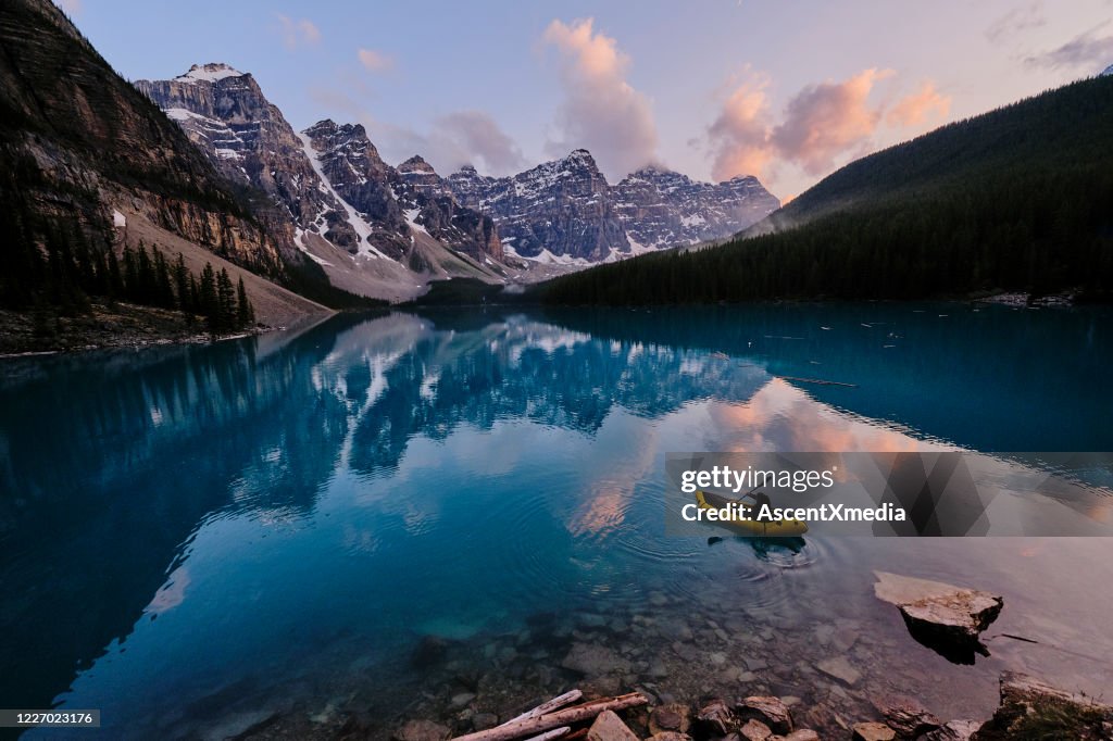 Young woman kayaks across mountain lake at sunrise