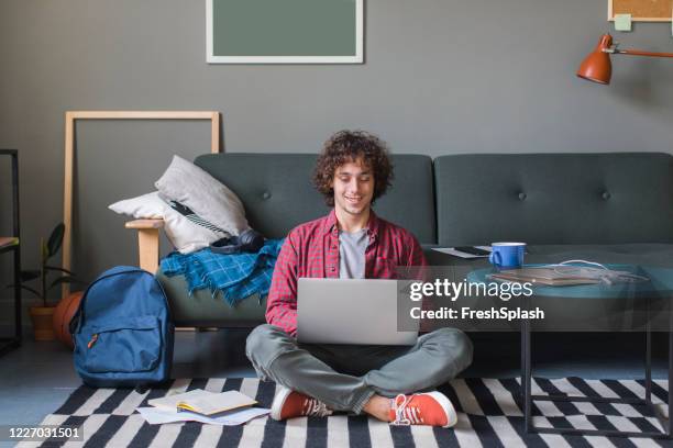 smiling college student sitting on the floor and using his laptop computer - teenager studying stock pictures, royalty-free photos & images