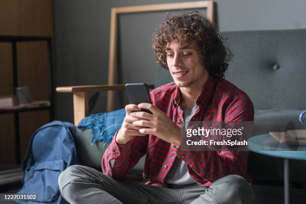 happy young man con una camisa de cuadros rojo casual usando su teléfono móvil en casa - checked shirt fotografías e imágenes de stock
