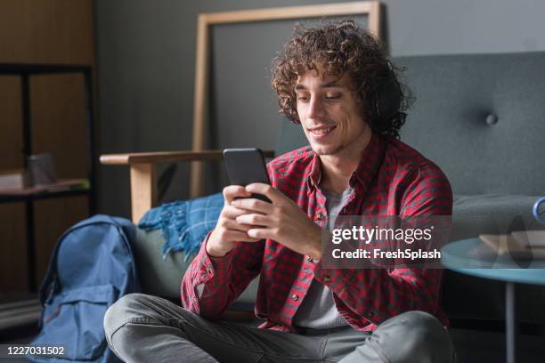 happy young man in a casual red checked shirt using his mobile phone at home - playing toy men stock pictures, royalty-free photos & images