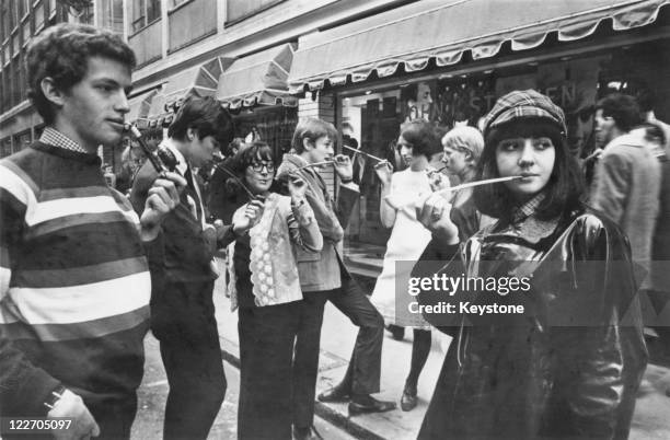 Fashionable young Londoners smoking pipes and cigarettes in long holders on a street in Soho, 9th February 1965. The craze began when a mod asked...