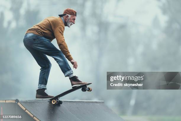 felice uomo anziano che fa skateboard su una rampa al parco. - skate foto e immagini stock