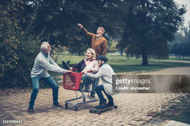 childish mature couples having fun at the park. - man pushing cart fun play stock pictures, royalty-free photos & images