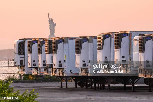 The Statue of Liberty is seen behind refrigeration trucks that function as temporary morgues at the South Brooklyn Marine Terminal during the...