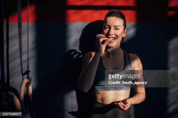 hermosa mujer en forma comiendo cacahuetes en el gimnasio - cacahuete alimento fotografías e imágenes de stock