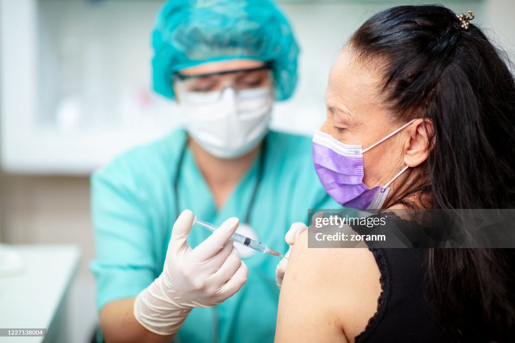 Ärztin in Schutzuniform in jiziert Impfstoff in den Arm des Patienten