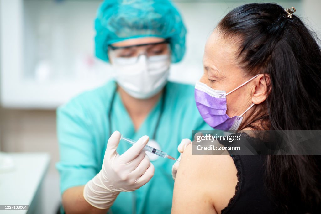 Female doctor in protective uniform injecting vaccine into patient's arm