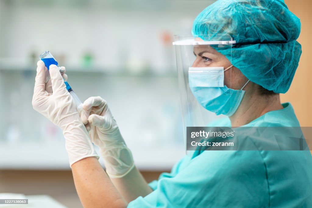 Female doctor pulling COVID-19 vaccine liquid from vial with syringe