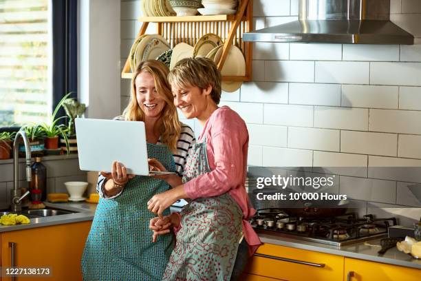 cheerful lesbian couple using laptop together in kitchen - couple laptop stock pictures, royalty-free photos & images