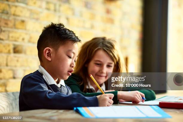 boy writing in workbook with sister watching at dining table - young girls homework stock-fotos und bilder
