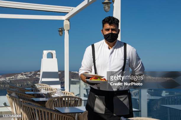 Portrait of a waiter serving the a la carte breakfast at the restaurant section with tables having distances between the tourists, instead of an open...