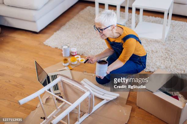 Mature woman watching DIY tutorials and painting a chair
