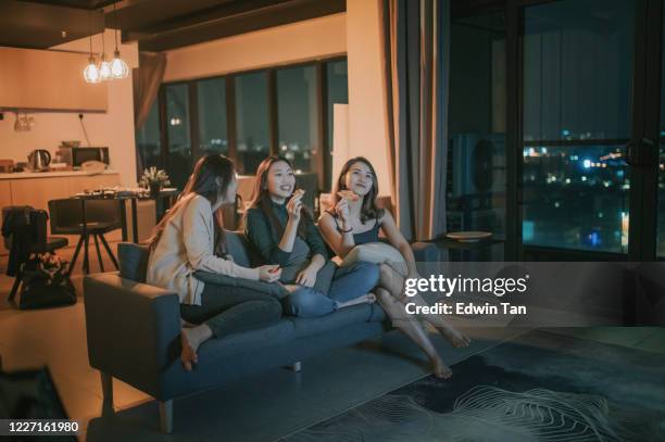 3 femmes chinoises asiatiques ayant la réunion de vendredi soir à l’appartement avec la nuit de film de tv appréciant le casse-croûte s’asseyant sur le sofa appréciant chaque compagnie appréciant chaque compagnie - sister stock photos et images de collection