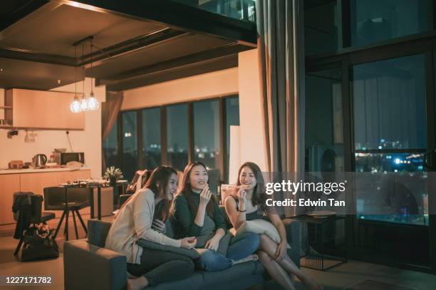 3 donne cinesi asiatiche che si radunano venerdì sera in appartamento con la serata del film tv godendosi uno spuntino seduto sul divano godendo di ogni compagnia - apartment living asian foto e immagini stock