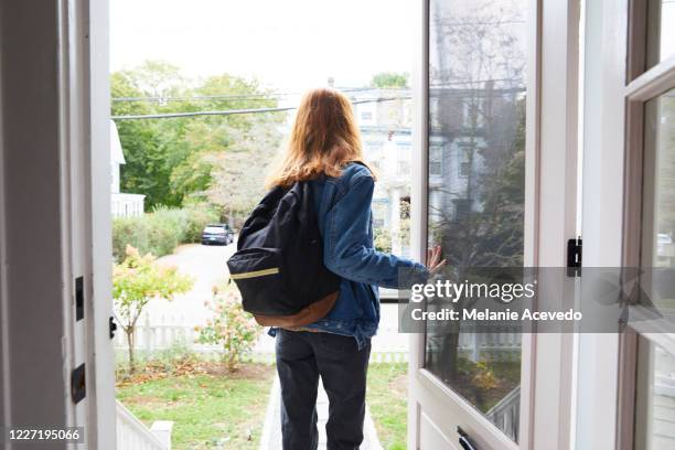 teenage girl walking out the front door of her house. back view of her leaving the house. she is on her way to school, wearing a back pack and holding the door open. - porta de tela imagens e fotografias de stock