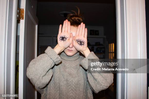 portrait of a teenage girl covering her eyes with her hands which have drawings of eyes on them. shot from the chest up. indoors. - hand gag foto e immagini stock