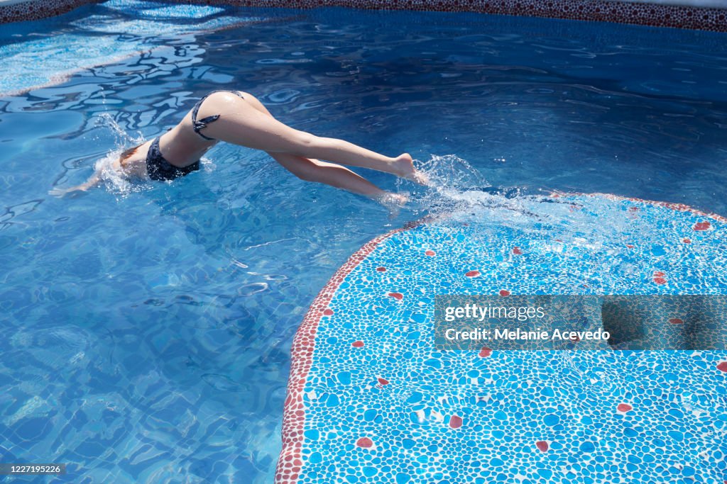 Teenage girl diving into a blue swimming pool in Mexico. She is alone in the pool.