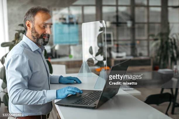 uomo d'affari che usa laptop con guanti protettivi in ufficio - rinviare la palla foto e immagini stock