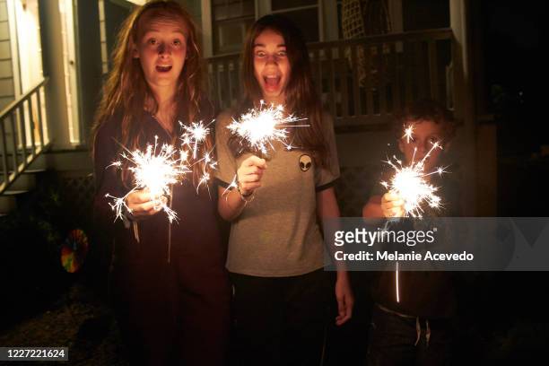 two teenagers and one small child playing with lit sparklers at night on the fourth of july. - garden night photos et images de collection