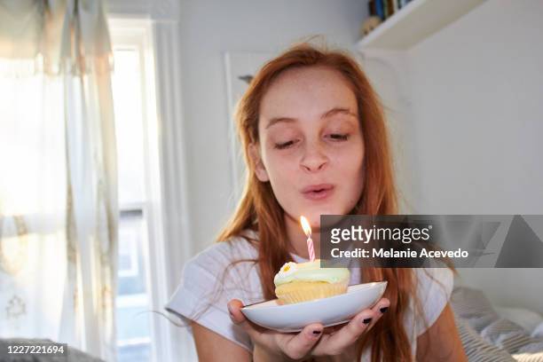 Teenage girl in her bedroom celebrating her birthday with a cupcake with a birthday candle in it. She is getting ready to blow out the candle.