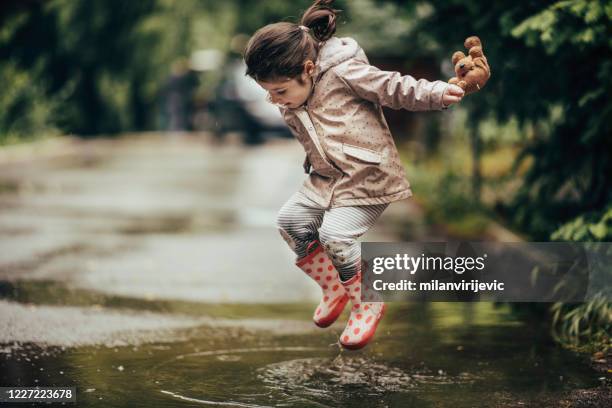 smiling little girl playing in a puddle stock photo - rain puddle stock pictures, royalty-free photos & images