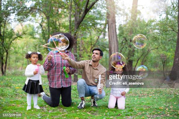 de gelukkige jonge multiethnic familie speelt met zeepbellen in een park. - bubbles happy stockfoto's en -beelden