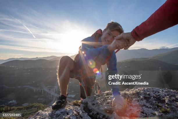 pov down arm to young man climbing up a rock face - climbing help stock pictures, royalty-free photos & images