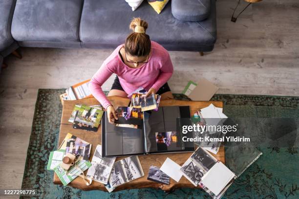mujer adulta joven añadiendo fotos a un álbum de fotos en casa - album de fotos fotografías e imágenes de stock