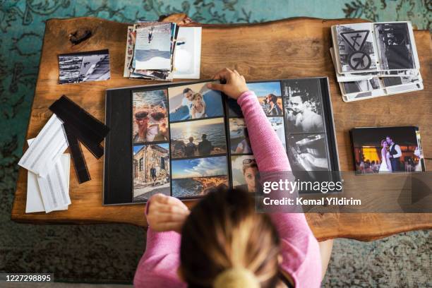 young adult woman adding photos to a photo album at home - scrapbook stock pictures, royalty-free photos & images