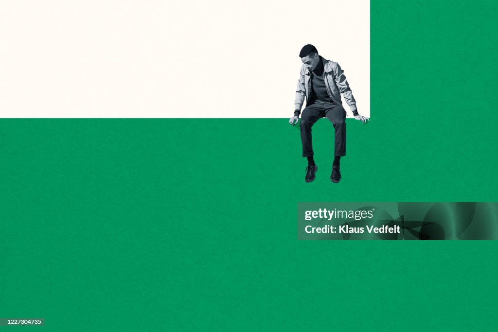 Dejected man sitting on wall while looking down