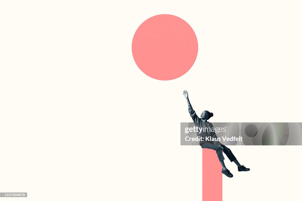Woman sitting on column while reaching for circle